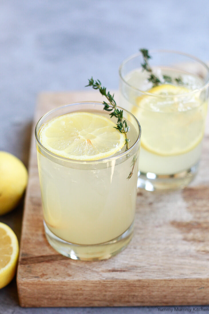 Two glasses of a homemade apple cider vinegar drink with lemon slices sit on a cutting board. 