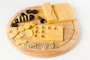 Теперь подготовим материал для нашей «поляны». Займёмся «пчёлками». Маслины нарезаем на кольца, из 1 шт. маслины получится 4 колечка, всего таким образом разрезаем 4 маслины для 2 пчёл (края нам не все понадобятся). Из сыра вырезаем тонкий пласт (по толщине примерно одинаковый с толщиной колец маслин). Формочкой (у меня насадка на кондитерский мешок) вырезаем из сыра кольца. Они должны получиться примерно такими, как и кольца из маслин. Также из сыра вырезаем «крылья» — всего 8 шт. Также вырезаем из маслин «головы» пчёлкам — одну маслину разрезаем поперёк на 2 части и каждую ещё вдоль (из 1 маслины получится 4 части, 2 нам понадобятся, а 2 нет).