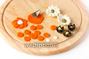 Теперь подготовим «цветы». Из яйца делаем зубчатые цветочки (1 яйцо на 2 цветка) — в центр которых выкладываем каперсы или зелёный горошек (или кусочек моркови), из маслин также вырезаем зубчатые цветы (в центр — кубик сыра), из колец моркови вырезаем насадкой для кондитерского мешка кольца, формируем цветок (3 шт.), в центре которых кружок яичного белка.