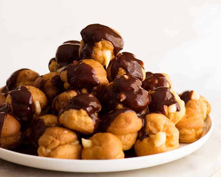 Pile of profiteroles filled with custard and drizzled with chocolate