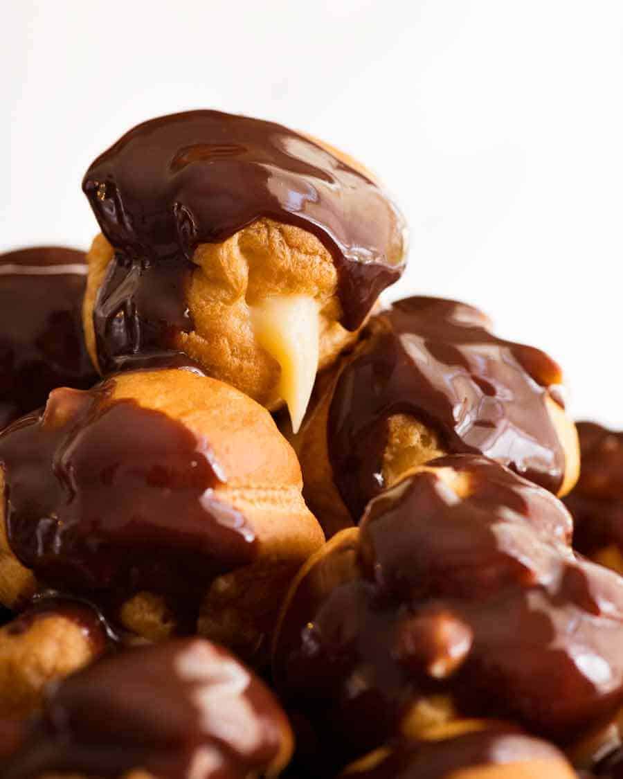 Close up of a pile of profiteroles filled with custard and drizzled with chocolate